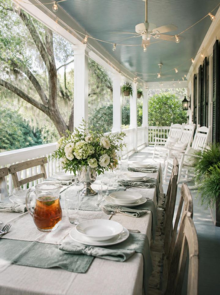 A long table set on the veranda under string lights and live oaks